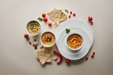 Tabakların görüntüsü, lezzetli humus kaseleri, taze sebzeler ve gri arka planda pita ekmeği.