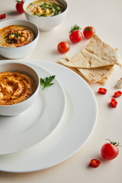 Selective focus of plates, bowls with delicious hummus, fresh vegetables and pita bread on grey 