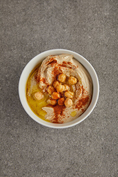 Top view of bowl with delicious hummus with chickpea and olive oil on grey background