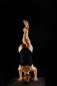 back view of girl in bodysuit doing eagle legs handstand exercise isolated on black 
