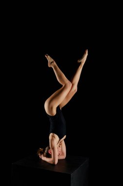 Çıplak ayaklı çekici bir kız yoga yapıyor. Siyahlara izole edilmiş amuda kalkıyor. 