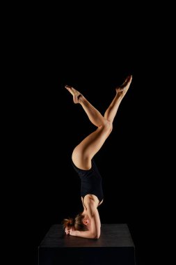 Çıplak ayaklı bir kız yoga yapıyor. Siyahların üstünde amuda kalkma egzersizi yapıyor. 