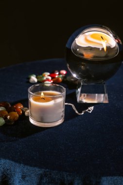 Kristal kürenin, mumların, fal taşlarının seçici odağı koyu mavi kadife kumaşın siyah üzerine izole edilmiş taşları anlatıyor.