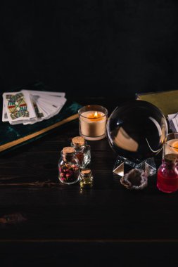 KYIV, UKRAINE - JANUARY 9, 2020: tarot cards and crystal ball with occult objects on wooden and black background clipart