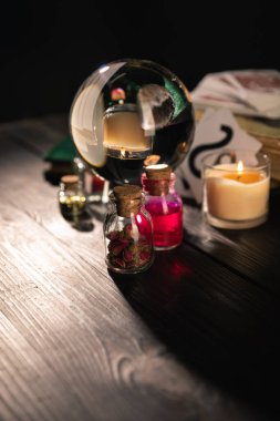 Selective focus of crystal ball, candle and jars of dried herbs and tincture isolated on black  clipart