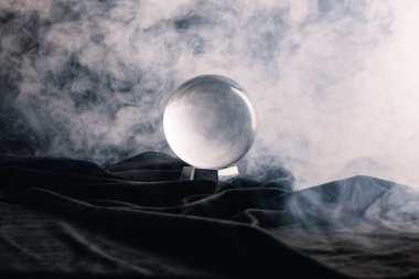 Crystal ball on textile with smoke on dark background clipart