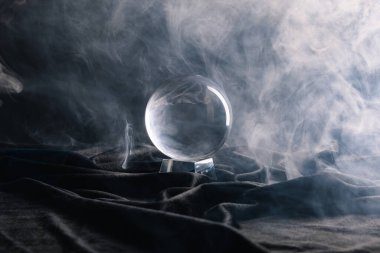 Crystal ball on black textile with smoke on dark  clipart