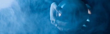 Cropped view of female hands with crystal ball and smoke around on dark blue background, panoramic shot clipart