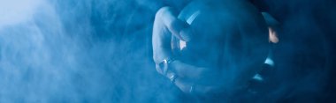 Cropped view of female hands with crystal ball and smoke around on dark blue background, panoramic shot clipart