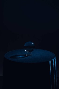 Yuvarlak masada kristal top, siyah arka planda koyu mavi masa örtüsü.