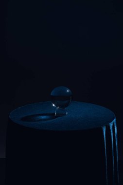 Crystal ball on round table with dark blue tablecloth on black background clipart