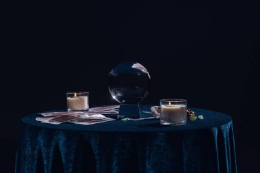 KYIV, UKRAINE - JANUARY 9, 2020: crystal ball with candles, tarot cards, stones and chain on round table isolated on black clipart