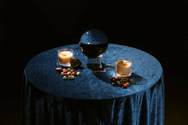 Хрустальный шар, свечи и фортуна говорят камни на темно-голубой ткани велюра изолированы на черном
