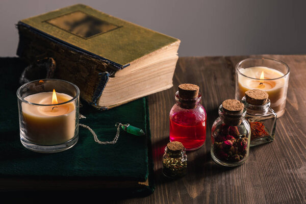 Jars with herbs and tincture, books, candles on wooden and grey background