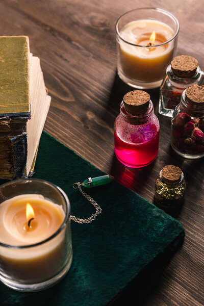Jars with magic herbs and tincture, books and candles on wooden background