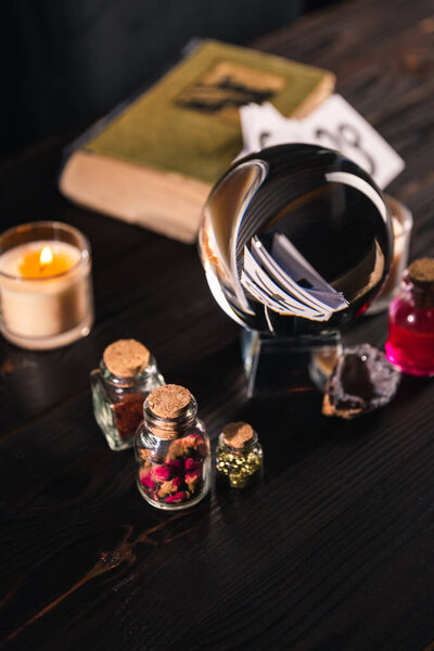 Selective focus of crystal ball, candle and occult objects on wooden background