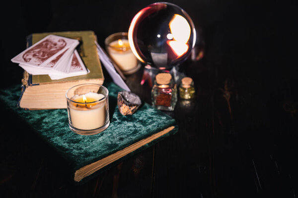 KYIV, UKRAINE - JANUARY 9, 2020: selective focus of crystal ball, books, candles, tarot cards and jars with dried herbs on dark background