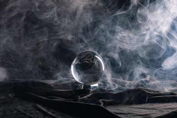 Crystal ball on black textile with smoke on dark background