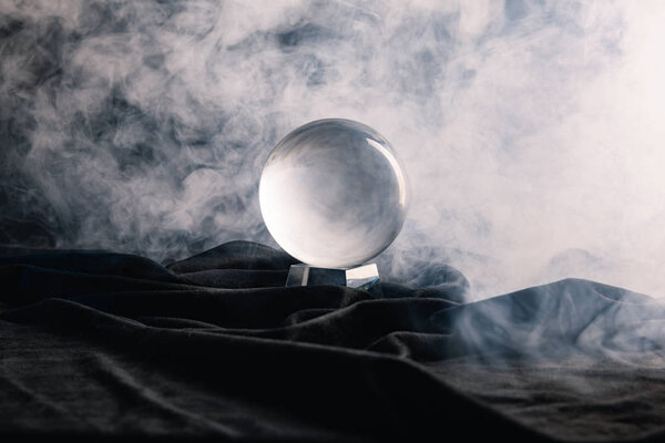 Crystal ball on textile with smoke on dark background