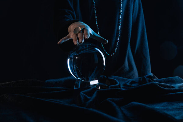 Cropped view of female hand touching crystal ball on black background