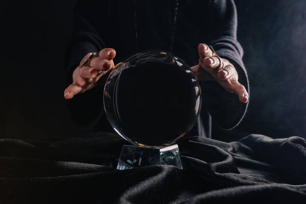 Partial view of female hands above crystal ball on black background