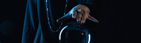 Cropped view of female hand touching crystal ball on black background, panoramic shot