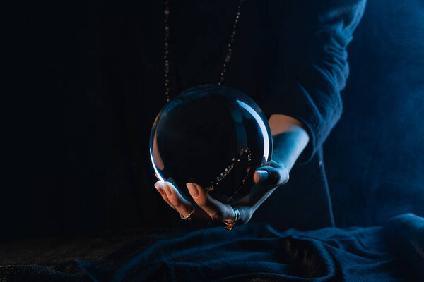 Partial view of crystal ball in female hand on dark blue