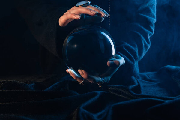 Partial view of witch with crystal ball on dark blue 