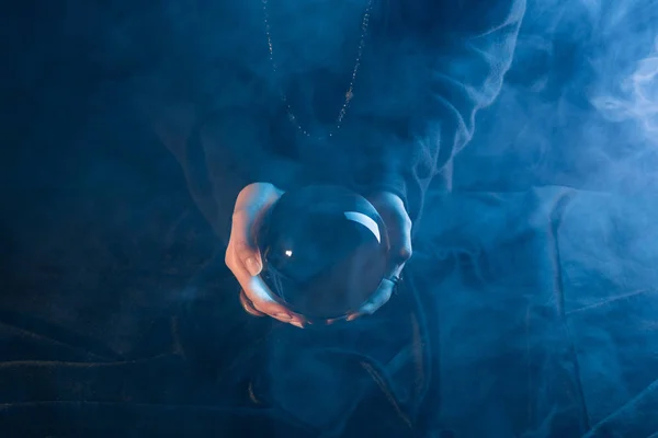 Vista Cortada Bruxa Segurando Bola Cristal Acima Mesa Azul Escuro — Fotografia de Stock