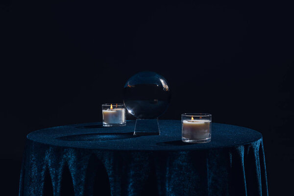 Crystal ball with candles on table isolated on black