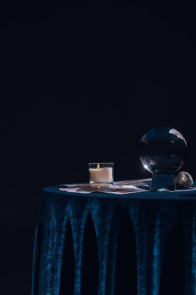 КИЕВ, УКРАИНА - 9 ЯНВАРЯ 2020: Хрустальный шар со свечами и оккультными предметами на круглом столе, изолированном на черном
