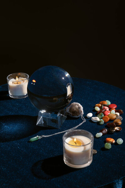 Хрустальный шар со свечами и оккультными предметами на круглом столе изолирован на черном
