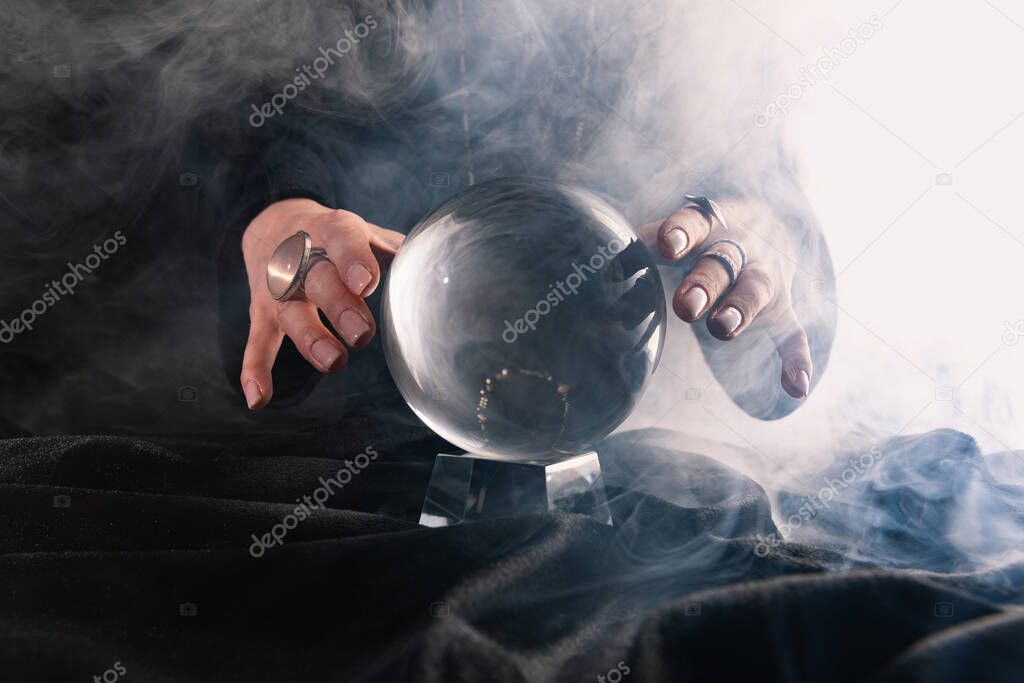 Partial view of female hands near crystal ball on dark background