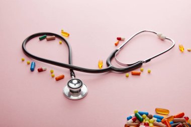 Yüksek açılı steteskop ve pembe üzerine parlak renkli ilaçlar. 