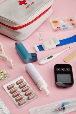 Pembe arka planda tıbbi nesnelerin yakınındaki ilk yardım çantasının yüksek açılı görüntüsü