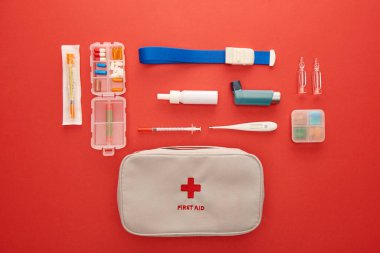 Flat lay with first aid kit, pills and medical objects on red background clipart