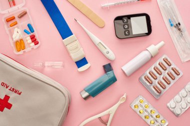 Pembe arka planda ilk yardım çantasının, ilaçların ve tıbbi eşyaların üst görüntüsü