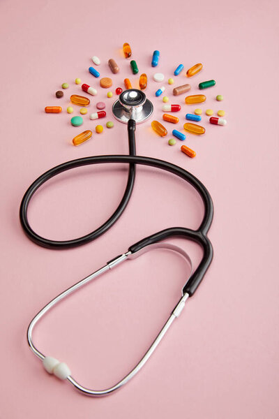 High angle view of stethoscope and bright medicines on pink 