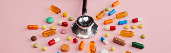 High angle view of stethoscope near bright colorful pills on pink background, panoramic shot