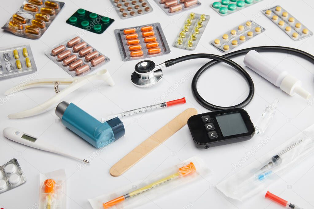 High angle view of colorful medicines, stethoscope, thermometer and medical objects on white