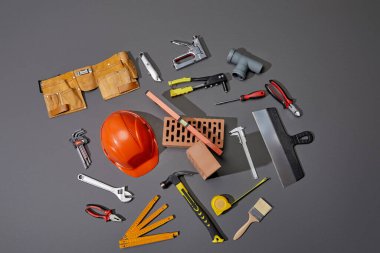 top view of bricks, tool belt, helmet and industrial tools on grey background clipart