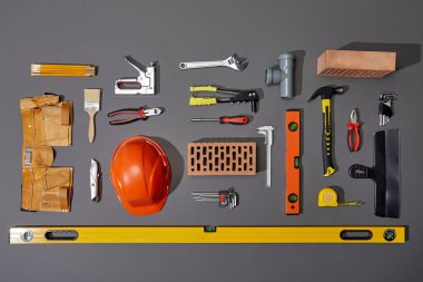 flat lay with bricks, orange helmet, tool belt and industrial tools on grey background clipart