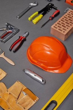 flat lay with orange helmet, tool belt, brick, industrial tools and brush on grey background clipart
