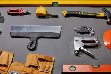 high angle view of spirit levels, pliers, measuring tape, hammer, putty knife, angle keys, stapler and tool belt on grey background  clipart
