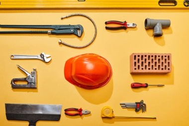 top view of industrial tools, helmet, plumbing hose and brick on yellow background clipart