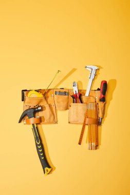 top view of tool belt with hammer, measuring tape, pliers, calipers, screwdriver and folding ruler on yellow background clipart