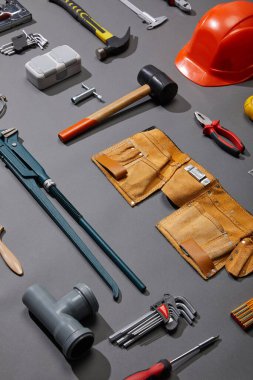 high angle view of tool belt, hammers, monkey wrench, putty knife, pliers, helmet, pipe connector, calipers, angle keys and brush on grey background clipart