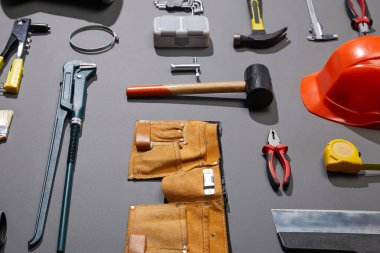 high angle view of tool belt, helmet, hammers, monkey wrench, putty knife, pliers, calipers, rivet gun and measuring tape on grey background clipart