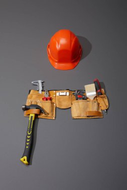 high angle view of helmet, tool belt with hammer, brush, pliers, calipers, angle keys and screwdriver on grey background clipart