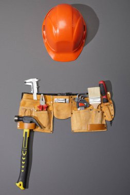 top view of helmet, tool belt with hammer, brush, pliers, calipers, angle keys and screwdriver on grey background clipart